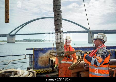 Fehmarn, Germany. 04th June, 2021. Drilling specialists Premslaw Niecieki (l-r) and Sergej Reinhardt remove an auger from the earth during a test drilling on a drilling platform in the Fehmarn Sound. The drilling is being used to plan the construction of the Fehmarnsund Tunnel between the Schleswig-Holstein mainland and the island of Fehmarn. The Fehmarnsund Bridge can be seen in the background. Credit: Gregor Fischer/dpa/Alamy Live News Stock Photo