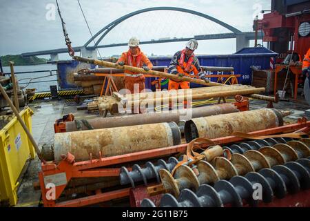 Fehmarn, Germany. 04th June, 2021. Premslaw Niecieki (l-r) and drilling technician Sergej Reinhardt dismantle the rods of a borehole on a drilling rig during test drilling in the Fehmarn Sound. The drilling is being used to plan the construction of the Fehmarnsund Tunnel between the Schleswig-Holstein mainland and the island of Fehmarn. The Fehmarnsund Bridge can be seen in the background. Credit: Gregor Fischer/dpa/Alamy Live News Stock Photo