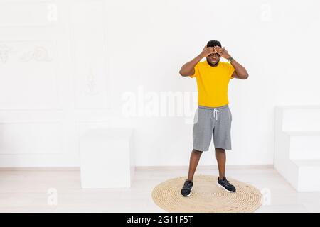 Tired afro american sporty man in bright yellow sportswear feeling exhausted after workout exercising at home using modern gadgets over white Stock Photo