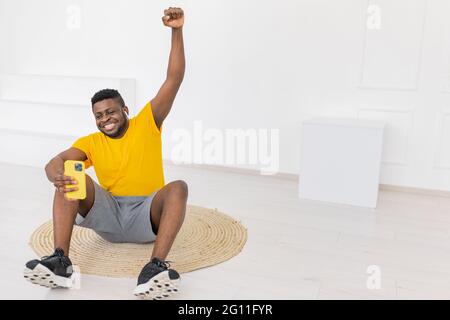 Full length portrait of african american guy hold mobile phone in yellow t-shirt isolated on white background. Young man doing selfie photo on smart Stock Photo