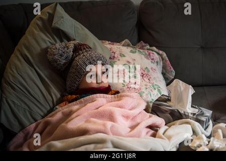 Canada, Ontario, Boy in knit hat lying on sofa covered with blanket Stock Photo