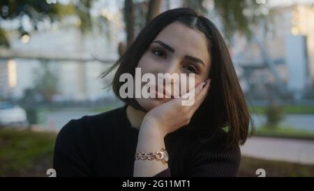 Beautiful young woman close-up portrait of joyful with, the wind waves your hair. Alone in park smiling looking at camera. Stock Photo