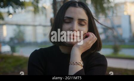 Beautiful young woman close-up portrait of joyful with, the wind waves your hair. Alone in park smiling looking at camera. Stock Photo