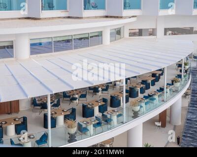 Open-air terrace hotel restaurant with wooden dining tables and blue chairs waiting for tourists with the view over the mediterranean sea in Ayia Napa Stock Photo