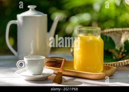 Ghee butter in glass jar on breakfast table with white teapot and cup. Stock Photo