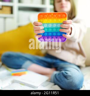 Teenage girl playing with rainbow pop-it fidget toy while studying