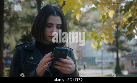 Young unhappy pretty woman wearing a leather jacket is dealing with the phone. Stock Photo