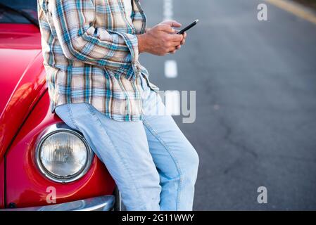 Standing unrecognizable man using phone outdoor - unrecognizable people with cellular smartphone chatting or texting with car in background - modern l Stock Photo