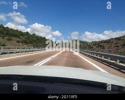 View of an empty mountainous road with right turn road sign taken from inside moving car. Stock Photo