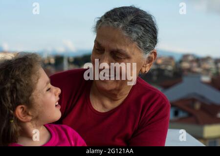 Grandmother and granddaughter are sitting on the balcony of their house and showing their love to each other. Selective Focus Faces Stock Photo