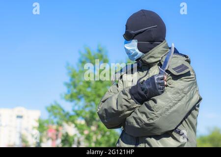 Modern dangerous and armed criminal in balaclava and medical mask among city streets Stock Photo