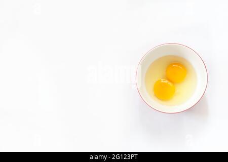 Raw eggs, top view of two raw eggs in bowl on isolated white background with space for text. Stock Photo