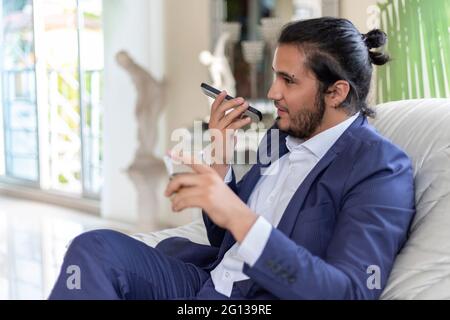 Young man sending voice message with cell phone. Home Office Stock Photo