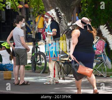 A Native American man dressed in Plains Indian regalia sells artworks and talks with tourists in the historic Plaza in Santa Fe, New Mexico. Stock Photo