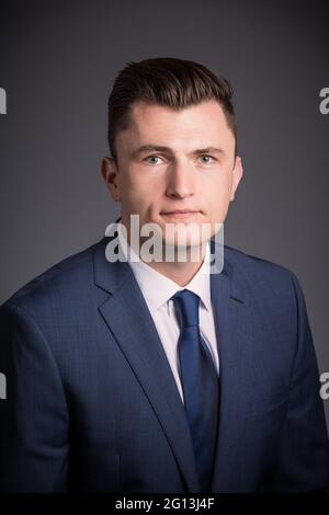 A young man in a corporate portrait. He is unsmiling as he looks at the camera, wearing a suit and tie in his headshot. Stock Photo