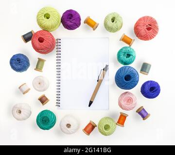 Multicolored balls and bobbins of woolen yarn, wooden thread sleeves on white isolated background. Notepad with pen. Needlework, handmade. view from a Stock Photo