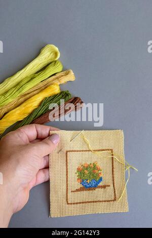Close up of woman's hand making cross-stitch on light-brown cotton canvas. Handmade embroidery, set of multi-colored threads. Copy space Stock Photo