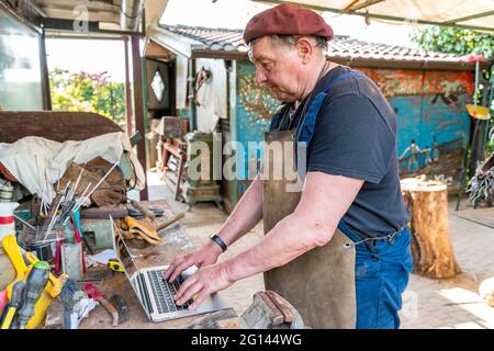 portrait of mature blacksmith. Worker on the computer in the laboratory in the countryside Stock Photo