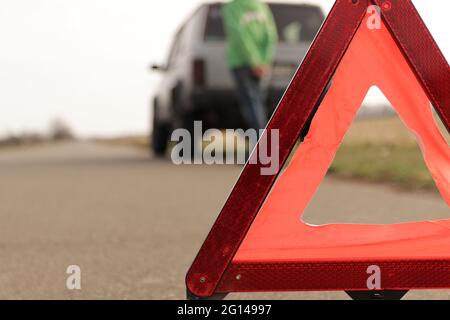 Red triangle of a stopped car on the road. An emergency stop sign mounted on the road against the background of stopped car. The concept of safe traff Stock Photo