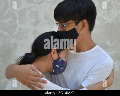 A pair of young lovers with dark cloth face masks are locked in a tender embrace during the global coronavirus pandemic. Stock Photo