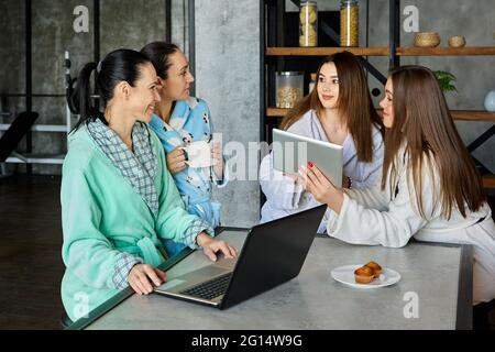Family is discussing something at breakfast using electronic devices, women are conferring sitting at table in dressing gowns. Stock Photo