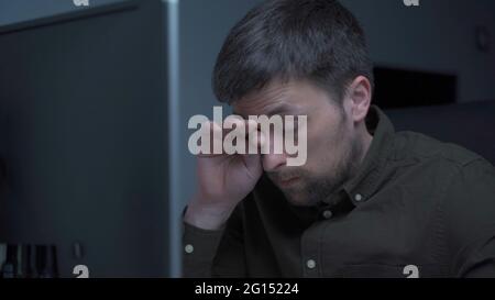 Home office. Handsome man working late at home. Tired young male feels pain, eye strain, dry irritated eyes, fatigue from working at monitor Stock Photo