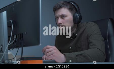 Young caucasian man working overtime at computer and eye fatigue from monitor in home office. Male having stressful time working on PC. Exhausted Stock Photo