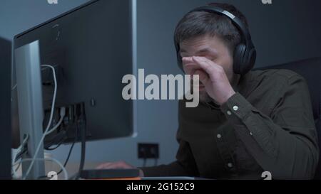 Home office. Handsome man working late at home. Tired young male feels pain, eye strain, dry irritated eyes, fatigue from working at monitor Stock Photo