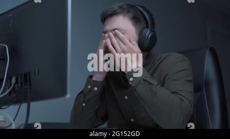 Home office. Handsome man working late at home. Tired young male feels pain, eye strain, dry irritated eyes, fatigue from working at monitor Stock Photo