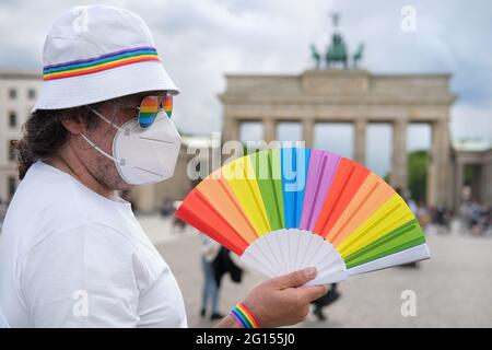 Mature Caucasian LGBT man in Berlin with rainbow fan and ribbon on white summer hat. Rainbow, symbol of LGBTQIA gay pride, diversity. Male activist is Stock Photo