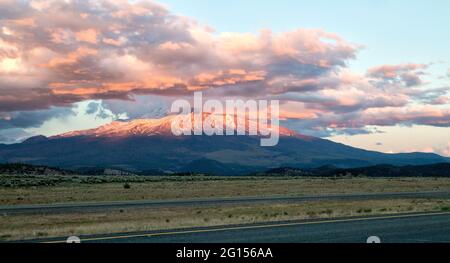 Cumulus clouds capping Mount Shasta & Shastina during sunset, field consisting of natural pasture land. Stock Photo