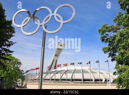 Montreal Olympic Stadium and inclined tower in Quebec, including multicolour waving flags and Olympic rings monument on the foreground, Canada Stock Photo