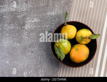 Tangerines with leaves in a bowl on a dark background. Top view, flat lay Stock Photo
