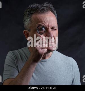 A man holds a magnifying glass in front of one eye looking through it with a very funny expression Stock Photo