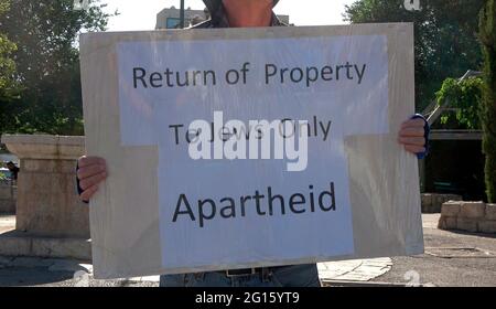 An Israeli left-wing activist holds a placard which reads 'Return of property to Jews only Apartheid' during a demonstration against Israeli occupation and settlement activity in Sheikh Jarrah neighborhood on June 04, 2021 in Jerusalem, Israel. The Palestinian neighborhood of Sheikh Jarrah is currently the center of a number of property disputes between Palestinians and right-wing Jewish Israelis. Some houses were occupied by Israeli settlers following a court ruling. Stock Photo
