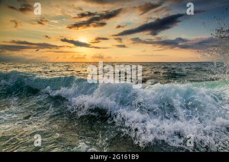 A Wave Is Breaking And Splashing As The Sun Sets On the Ocean Horizon Stock Photo