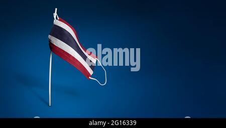 Waving flag of Thailand painted on medical mask on pole. Concept of The banner of the fight against the epidemic coronavirus COVID-19. Copy space Stock Photo