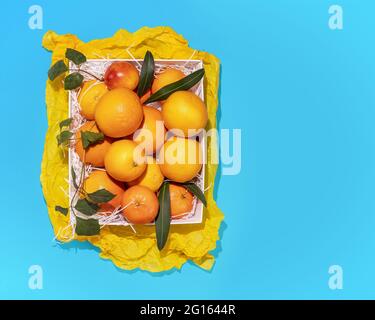 Horizontal, summer, fruits composition with fresh oranges in a white box on a blue background with copy space. Healthy, season, farm foods Stock Photo
