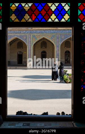 Two women in the courtyard of the Nasir-ol-Molk mosque (Pink Mosque) seen from the stained glassed winter prayer hall. Shiraz, Fars Province,  Iran Stock Photo