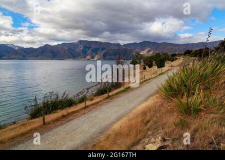 Lake Hawea in the Otago region of New Zealand's South Island. A gravel road runs along the shoreline Stock Photo