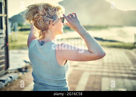 Back view of a young blonde caucasian woman with a tatoo in is nape outdoor in a beach area in a sunny day. Stock Photo