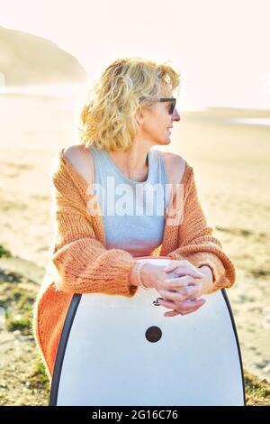 Portrait of a young mature blonde caucasian woman outdoor in a beach with a bodyboard and sunglasses in a sunny day. Stock Photo