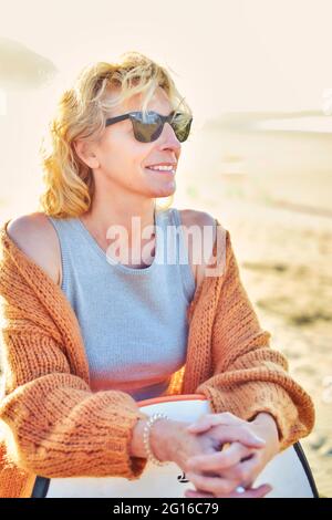 Portrait of a young mature blonde caucasian woman outdoor in a beach with a bodyboard and sunglasses in a sunny day. Stock Photo