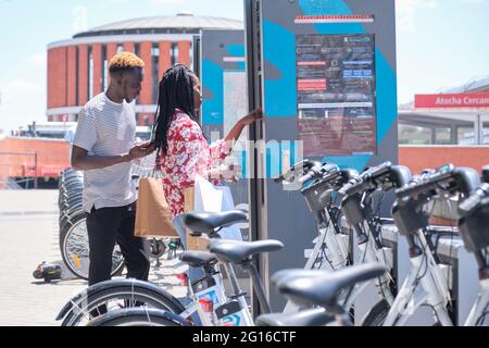 Madrid, Spain. May 29, 2021: Young african tourists renting a bike at a bicycle rental service machine. Stock Photo