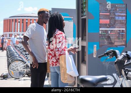 Madrid, Spain. May 29, 2021: Young african tourists renting a bike at a bicycle rental service machine. Stock Photo