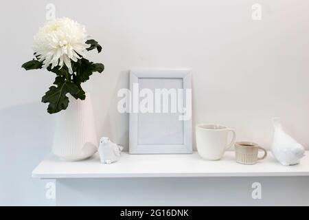 Large chrysanthemum in a glass vase. Photo frame with place for text, two corrugated cups with coffee and ceramic figurines of birds on the table. Off Stock Photo