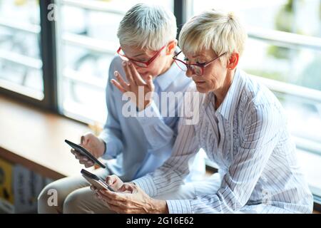 Two elderly business women of similar appearance using smartphones at the break in a relaxed atmosphere at workplace. Business, office, job Stock Photo