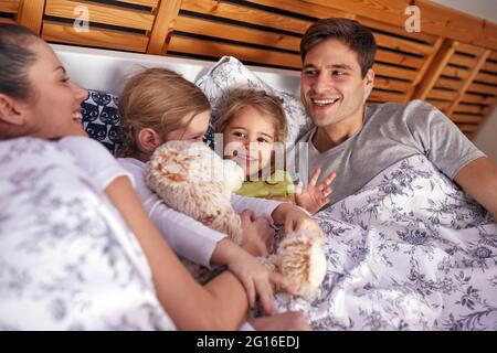 A little girls enjoying lying with their parents in the bedroom in a cheerful atmosphere at home. Family, together, home Stock Photo