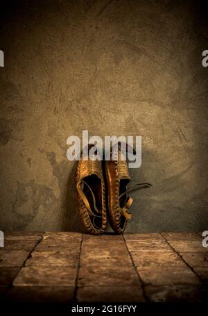 Old rustic  footwear made of leather on antique tiles and concrete wall background. Vintage clothes idea. Old national shoes. Stock Photo