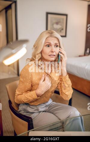 Blonde pretty woman sitting talking on the phone and looking stressed Stock Photo